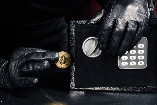 Male hand stealing golden bitcoin from safe