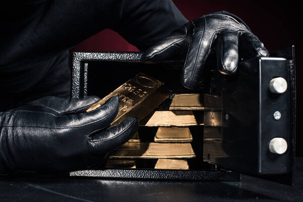 Cropped view of thief stealing gold ingots from safe