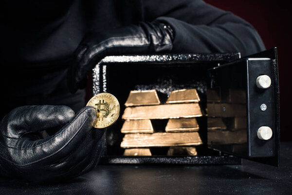 Cropped view of thief stealing gold bullions and bitcoin from safe