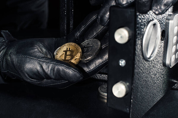 Thief hand stealing golden bitcoin from safe