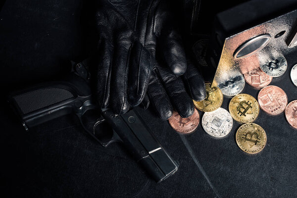 Black gloves and gun by open safe with bitcoin 