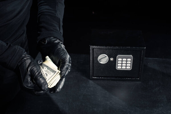 Close-up view of robber in gloves taking dollars from safe