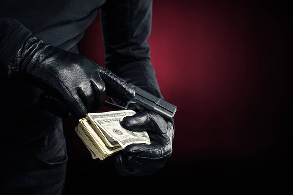 Cropped view of gun and dollars in hands of robber