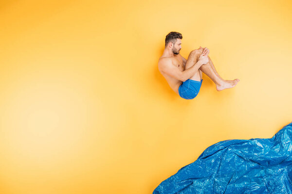 Красивый молодой человек в шортах, прыгающий в воображаемое море на желтом
 