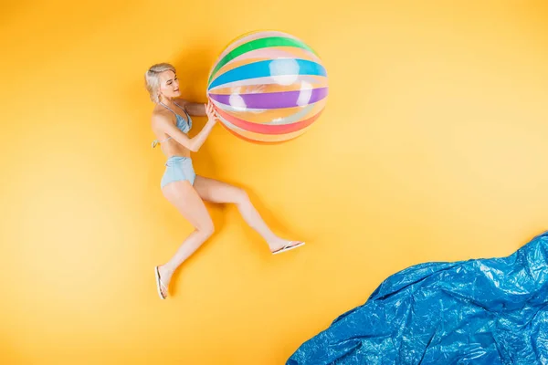 美丽的年轻女子在泳装和翻转拖鞋持有充气球在想象海滩 — 图库照片