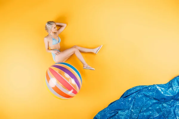 美丽的女孩穿着泳装和触发器坐在充气球在想象海滩 — 图库照片