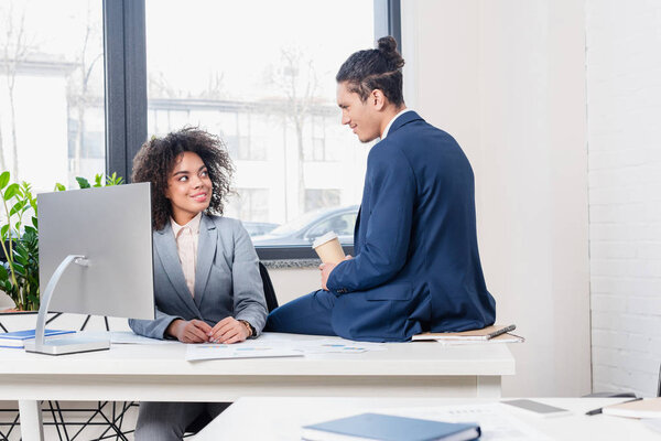 Woman by computer and man with coffee cup discussing business project