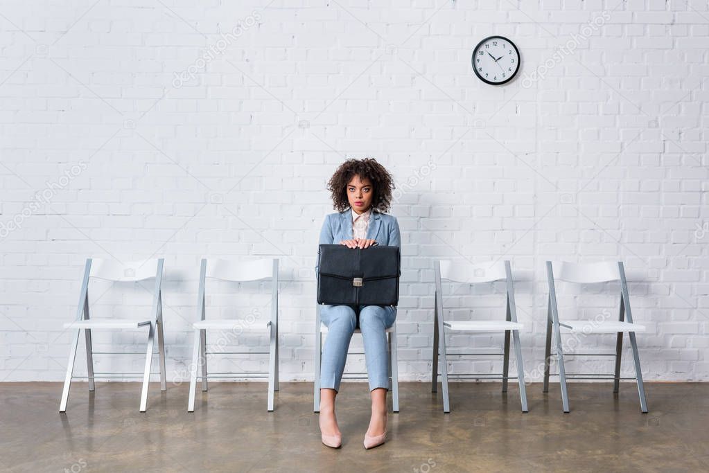 Tense businesswoman with briefcase sitting on chair and waiting