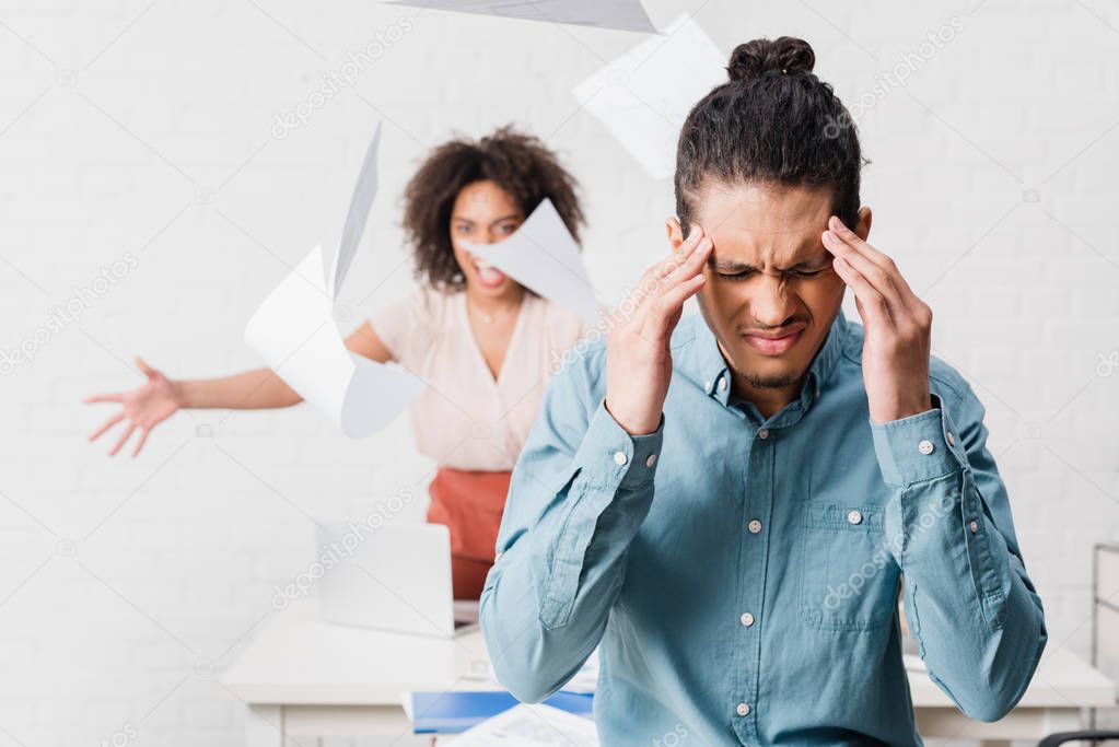 Businessman suffering from headache while his female colleague yelling in office