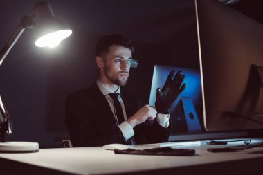 Karanlıkta masada bilgisayar ekranında bakarken eldiven giymiş hacker portresi