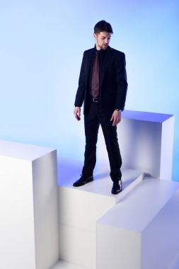 businessman in black suit standing on white block isolated on blue clipart