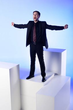 businessman in black suit with outstretched arms standing on white block isolated on blue clipart