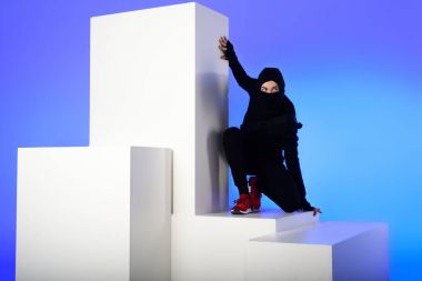 Ninja izole mavi beyaz blok üzerinde duran arkasında katana ile siyah giyim