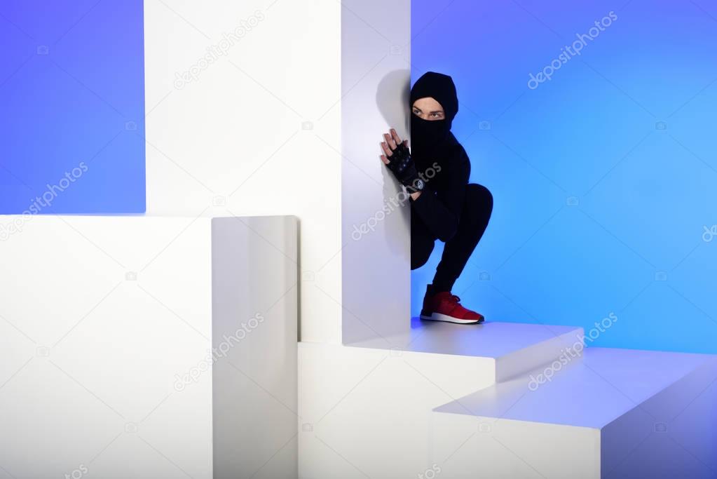 ninja in black clothing hiding behind white block isolated on blue