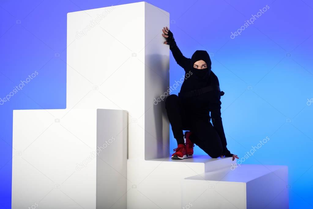ninja in black clothing with katana behind standing on white block isolated on blue