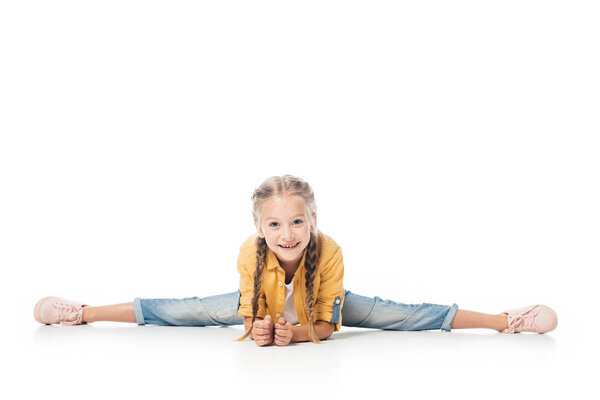 smiling little child stretching, doing split and looking at camera isolated on white