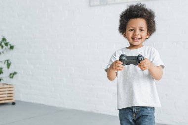 gülümseyen sevimli Afro-Amerikan çocuk evde joystick ile ayakta
