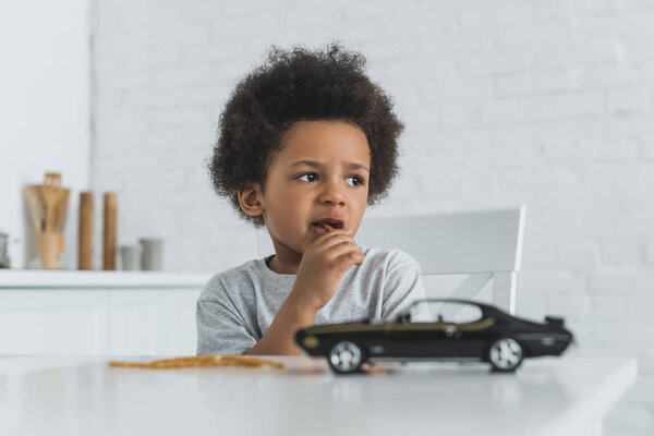 adorable african american boy eating crispy breadsticks at home