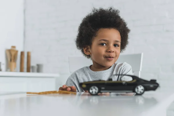 Adorable Afroamericano Chico Sentado Mesa Con Coche Juguete Mirando Cámara — Foto de Stock