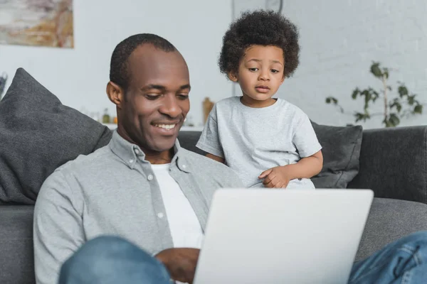 Africká Americká Syna Sledovat Jak Otec Doma Pomocí Přenosného Počítače — Stock fotografie