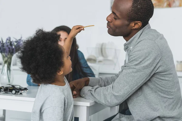 African American Son Feeding Father Crispy Breadsticks Home — Stock Photo, Image