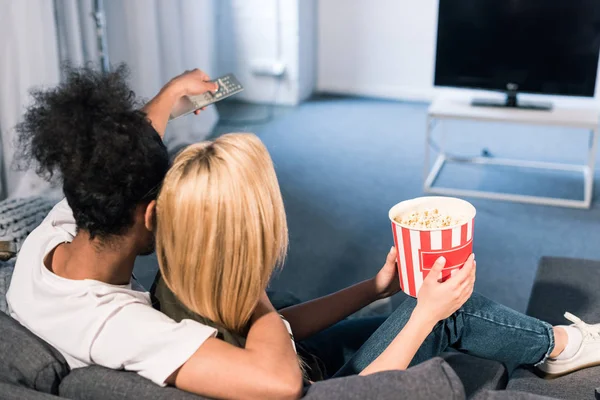 Visão Traseira Casal Multirracial Com Pipocas Assistindo Filme Juntos Casa — Fotografia de Stock