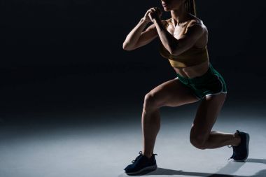 cropped view of sporty female bodybuilder doing lunges, on black    clipart
