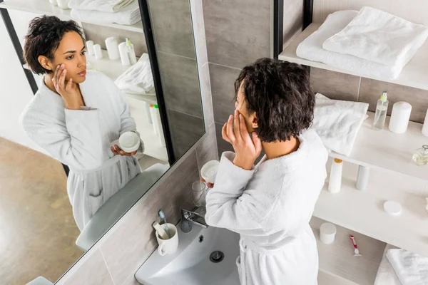 Mujer Afroamericana Aplicando Crema Antiarrugas Cosmética Cara Mirándose Espejo Baño —  Fotos de Stock