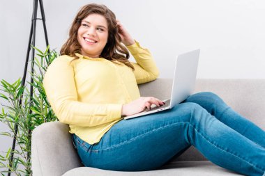 evde koltukta istirahat dizüstü bilgisayar ile gülümseyen genç kadın