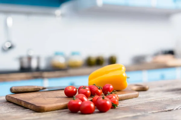 selective focus of fresh cherry tomatoes and bell pepper on tabletop with wooden cutting board and knife