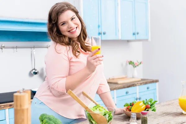 自宅のキッチンでジュースのガラスと太り過ぎの笑顔の女性の肖像画 — ストック写真