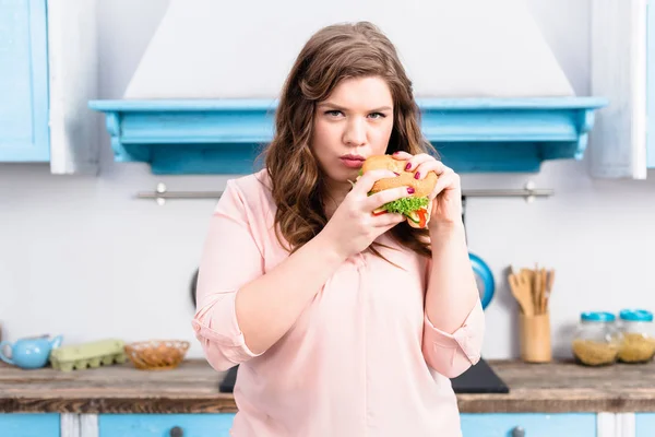自宅の台所で手でハンバーガー若い肥満女性の肖像画 — ストック写真