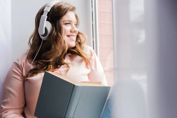 Smiling Woman Headphones Book Sitting Windowsill Home — Free Stock Photo