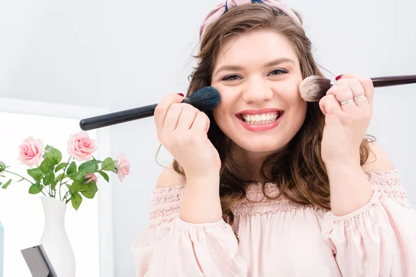 Atractiva Joven Con Pinceles Maquillaje Las Manos Mirando Cámara Casa —  Fotos de Stock