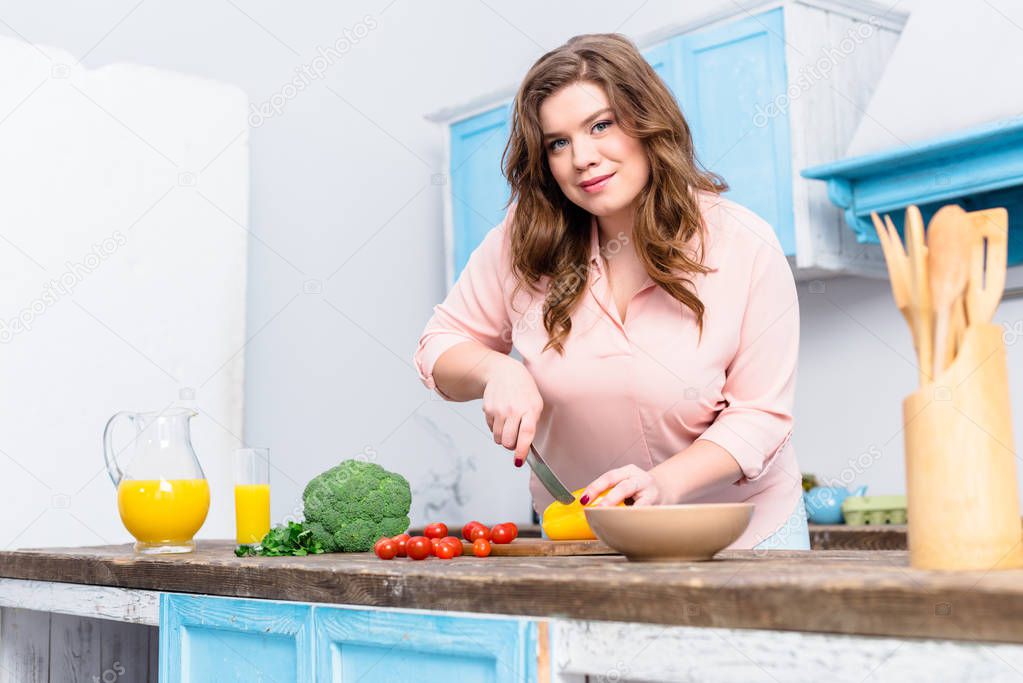 overweight woman cutting vegetables for salad in kitchen at home