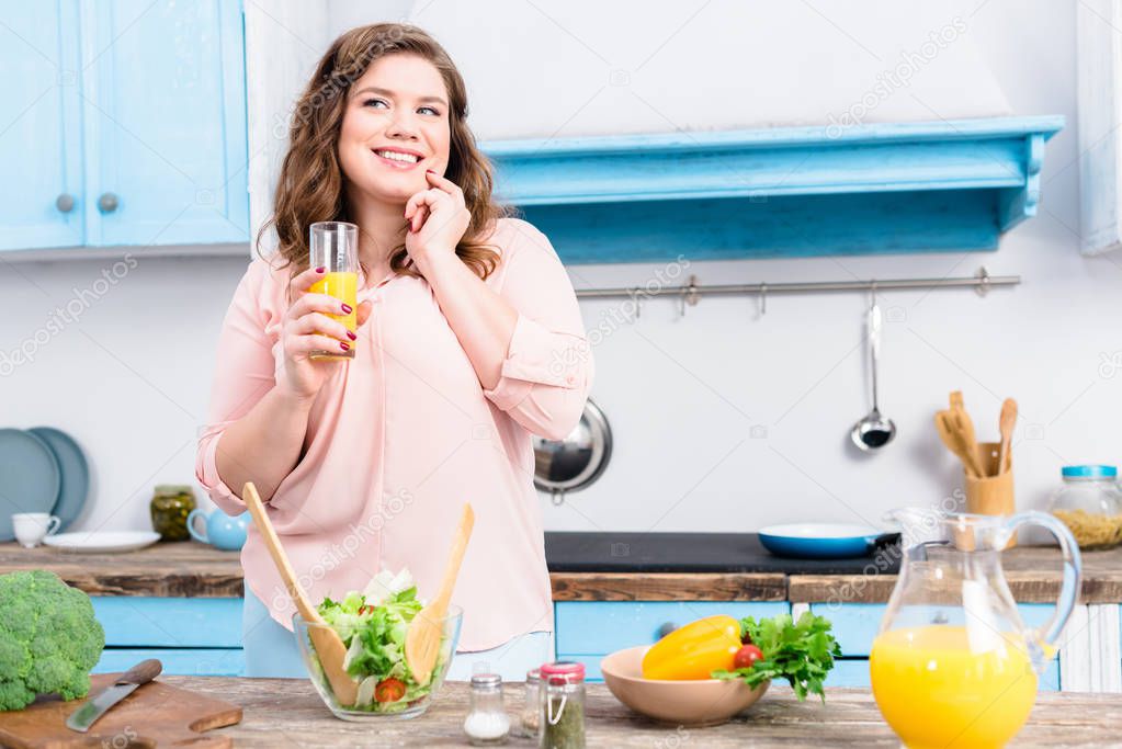 portrait of overweight smiling woman with glass of juice in kitchen at home