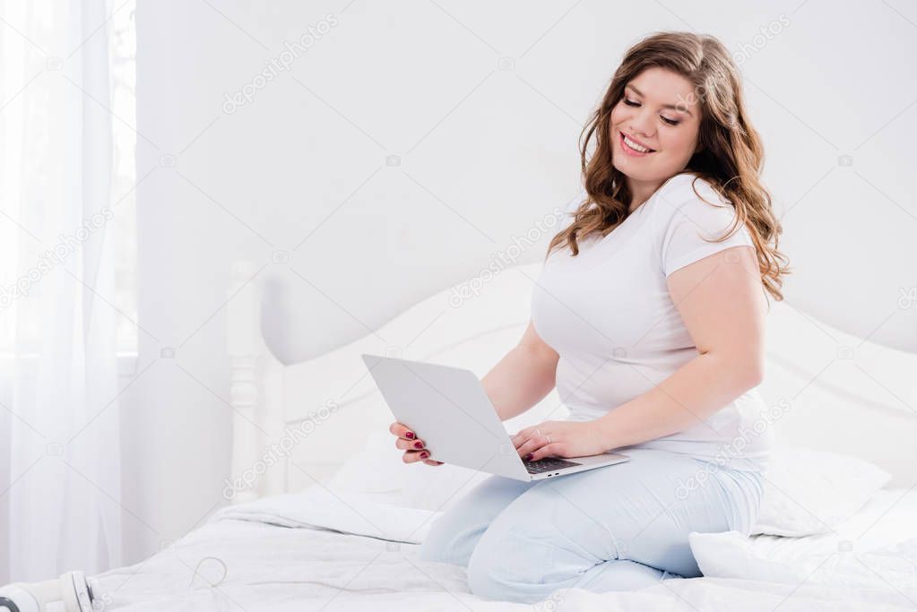 smiling woman in pajama using laptop on bed at home