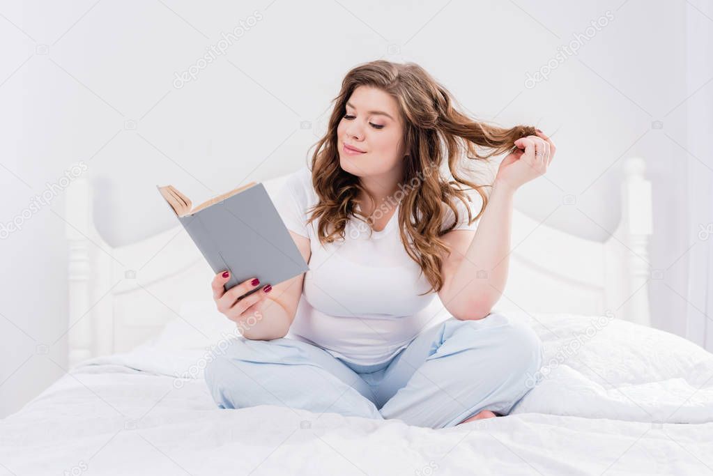 young woman in pajama reading book on bed at home
