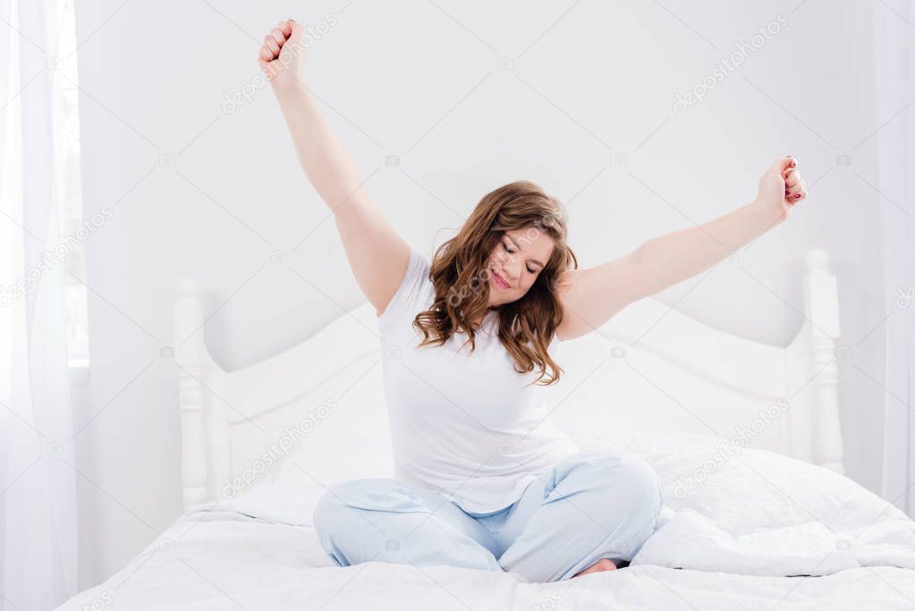 young woman in pajama stretching in morning on bed at home