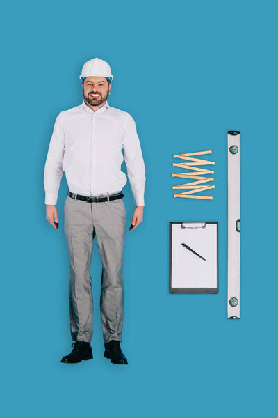 top view of builder man in helmet with clipboard, building level and collapsible meter isolated on blue background