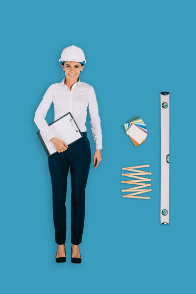 top view of female builder with clipboard, collapsible meter and building level isolated on blue background