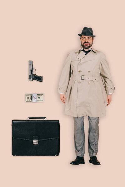 верхний вид мужчины-убийцы в шляпе с пистолетом, деньги и портфель изолированы на розовом фоне

