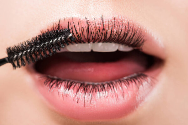 cropped image of woman applying black mascara on eyelashes in mouth isolated on white