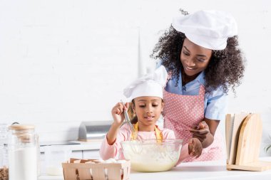 Afrika kökenli Amerikalı anne ve kızı yemek tarifleri ile mutfak hamur karıştırma chef şapka içinde