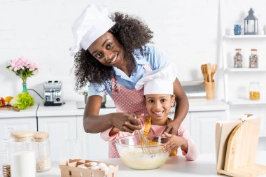 Afrika kökenli Amerikalı anne ve kızı mutfak üzerinde çırpma teli ile hamur karıştırma chef şapka içinde