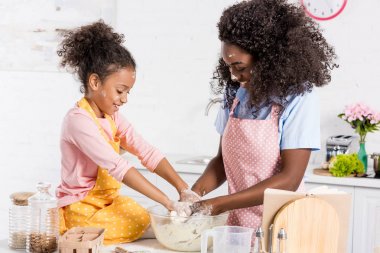 happy african american mother and daughter kneading dough on kitchen clipart