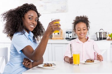 Afrika kökenli Amerikalı anne ve kızı yemek odasında kahvaltı krep ve portakal suyu ile