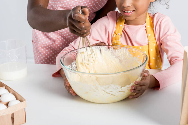 partial view of african american mother and daughter mixing dough with whisk on kitchen