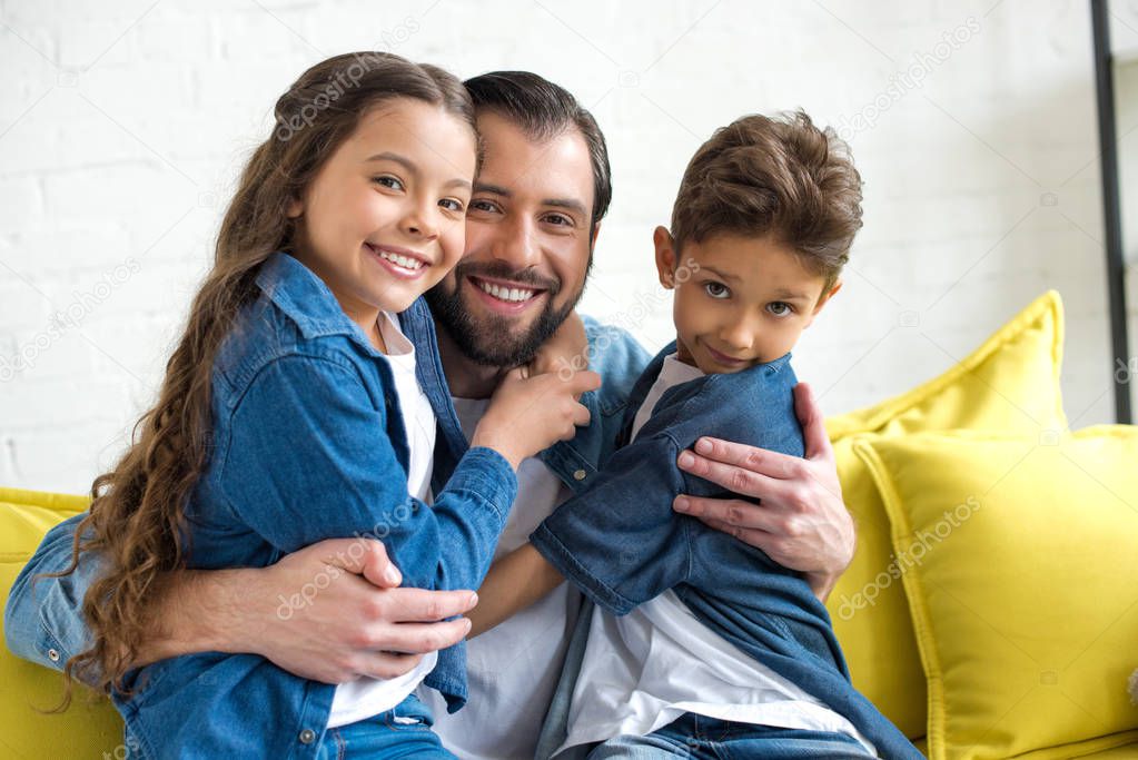 happy father hugging adorable little children and smiling at camera together at home