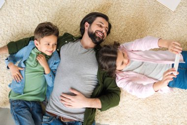 bir baba ile iki sevimli çocuk halı ve alma selfie smartphone ile yalan Üstten Görünüm